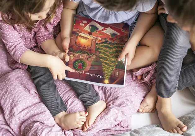 Tres niños sujetan el libro para colorear Navidades Mágicas, con un árbol de Navidad iluminado en la portada.