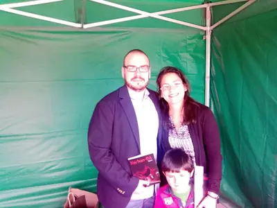 Dan S. V. posa con un ejemplar de Xerhon-Ra junto a una mujer sonriente y un niño, dentro de una carpa verde.