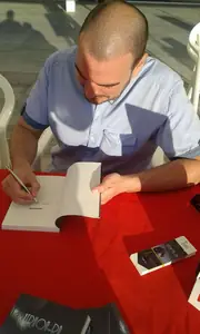 Vista desde arriba de Dan S. V. escribiendo una dedicatoria en un ejemplar de Xerhon-Ra, junto a un taco de marcapáginas.
