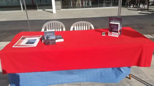 Mesa de mantel rojo con ejemplares de Xerhon-Ra y un cartel de libro recomendado, preparada para una firma al aire libre.